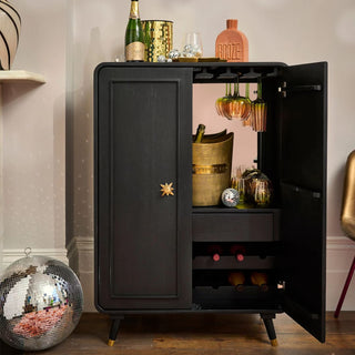 A picture of a black open cabinet with a champagne bucket and drink glasses in it. There is also a champagne bottle on top of it with a drinks decanter that says 'booze' on it. 