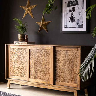 A leopard print sideboard with three sliding doors, against a matt black wall, styled with a green plant