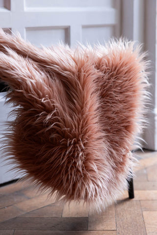 A pale pink sheepskin rug draped across a wooden chair