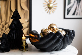 A giant bowl made of two giving hands in black, holding gold disco balls 