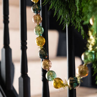 A black banister with a gold, green and black bauble garlands draped over it. 