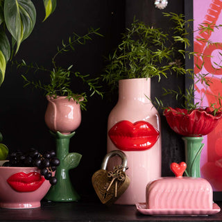 a flower vase styled pink and red lips homeware including a bowl, vase and butter dish, styled against a black background 