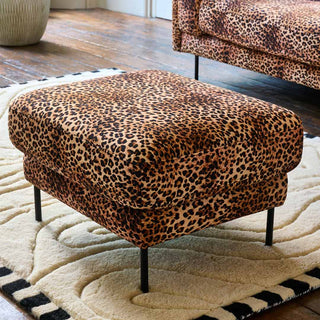 The Grace Foot Stool in Leopard Love Velvet Natural, styled in a living room on a rug in front of a leopard print sofa.