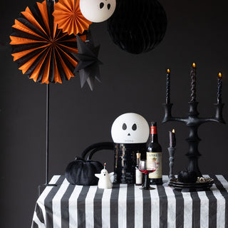 A cream velvet pumpkin displayed on some books with a leaf garland and two candlestick holders with lit candles in, on a black and wooden sideboard.