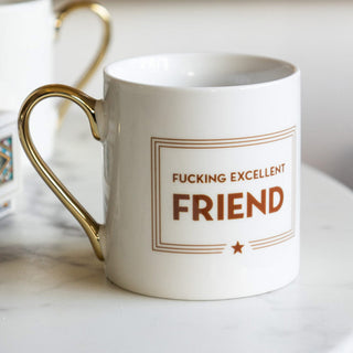 A white and gold mug with a bold print across the front saying 'fucking excellent friend'.