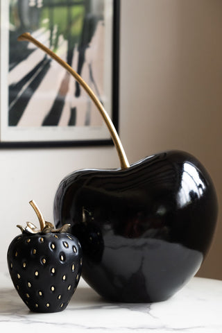 Large black cherry ornament on a side table with a small strawberry ornament 