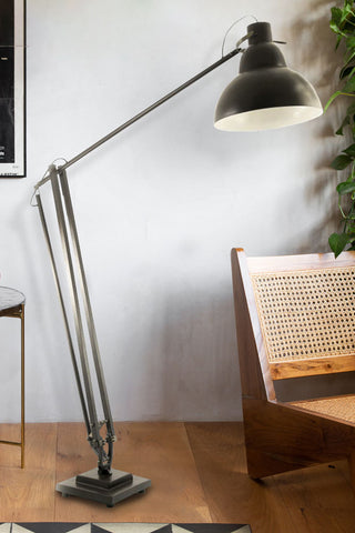 Black metal floor lamp with domed black shade styled next to a wooden chair and plant 