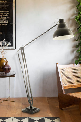 Black metal floor lamp styled next to a wooden chair, with the edge of a metal and glass coffee table peeping into shot 