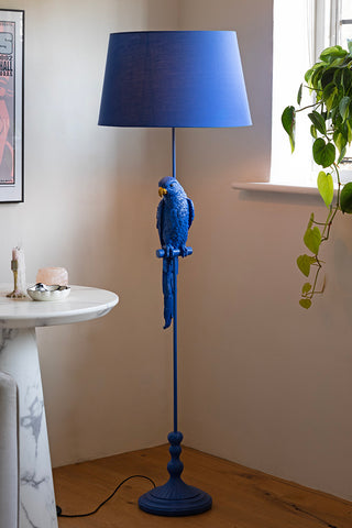 The Bold Blue Parrot Floor Lamp with Shade styled with a side table, on a wooden floor.