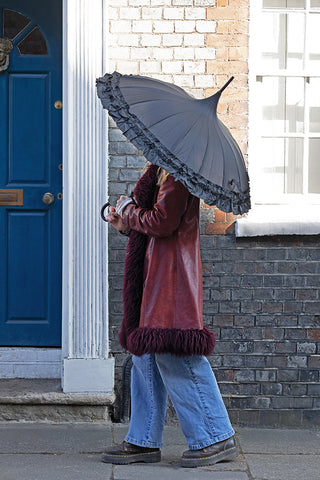 Lifestyle image of the Boutique Black Frilled Edge Umbrella being held outside a townhouse with a blue door.