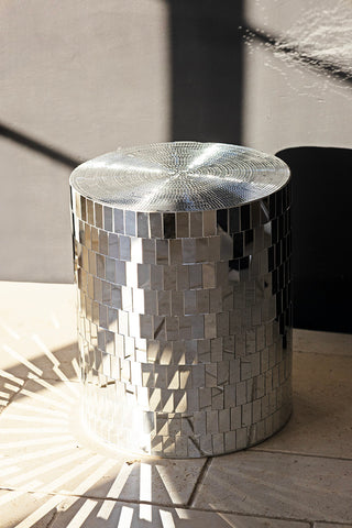 The Silver Disco Ball Mirrored Side Table styled on a tiled floor with sunlight creating reflections around it.