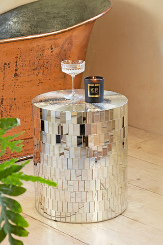 The Silver Disco Ball Mirrored Side Table styled next to a bath and plant, with a glass and lit candle on.