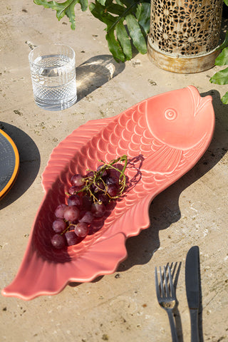 The Fish-Shaped Ceramic Serving Dish styled on an outdoor table with grapes inside, surrounded by various tableware.