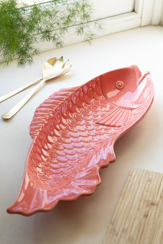 The Fish-Shaped Ceramic Serving Dish styled on a window ledge with a wooden board, salad servers and a plant.