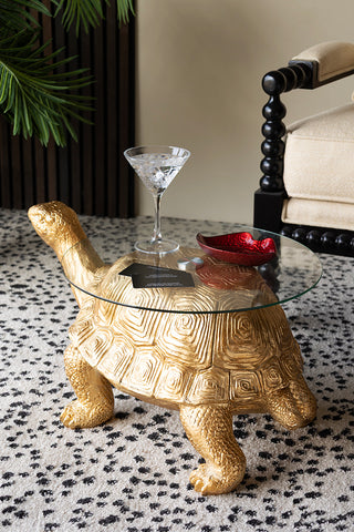 The Gold Tortoise Side Table seen from the back, styled with a glass and trinket dish on.