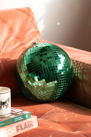 The Green Disco Ball styled on a sofa with some books and a mug.