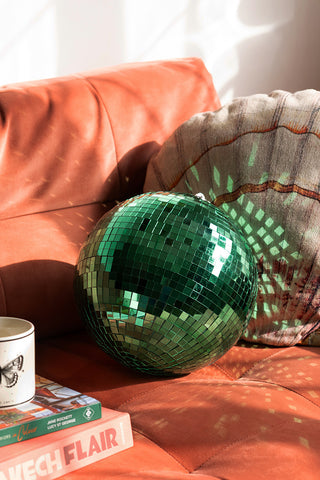 The Green Disco Ball styled on a sofa with a cushion, some books and a mug.