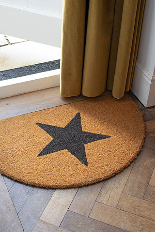 The Half Moon Star Doormat styled on a wooden floor by an open door, with a door curtain in the background.