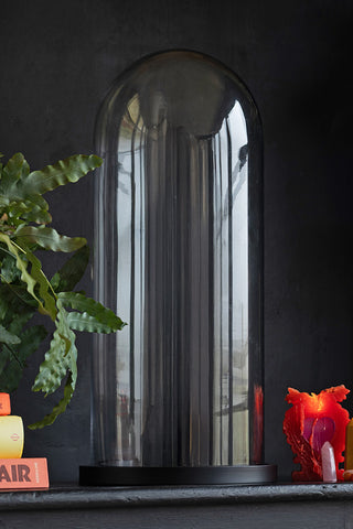 The Large Glass Dome Ornament styled on a black sideboard surrounded by books, a plant, a lit candle and some crystals.