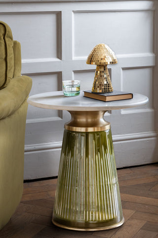 The Green Tapered Glass & Marble Side Table styled with a glass, book and ornament on, next to a sofa.