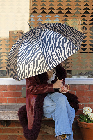 Lifestyle image of the Metallic Gold Zebra Print Umbrella being held outside a house.