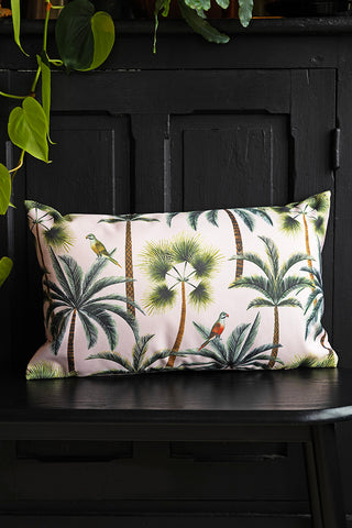 The Palm Print Outdoor Cushion styled on a black bench with greenery inside.