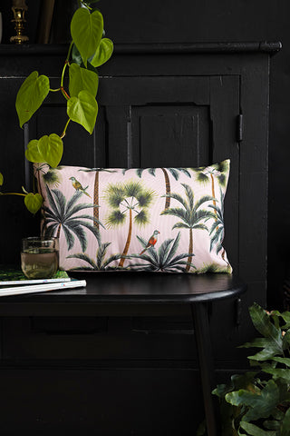 The Palm Print Outdoor Cushion styled on a bench with some magazines and a glass of water.