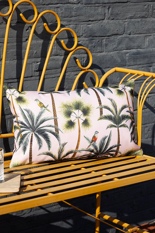 A beautiful palm and parrot print cushion on a yellow garden bench. The cushion is an outdoor cushion meaning it is weatherproof.