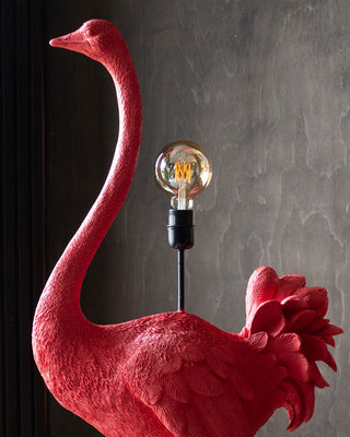 A bright pink ostrich floor lamp that stands around five foot tall. The Ostrich has a large bulb on its back.