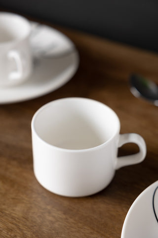 The Female Face Coffee Cup styled on a wooden table with other cups and saucers and a spoon.