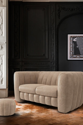 The Bowie Medium Sofa In Luxe Needlecord Velvet Natural Whisper styled in front of a dark wall with an art print on, next to a matching footstool.