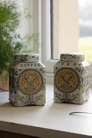 The Set of 2 Ceramic Tea & Coffee Storage Jars styled on a window ledge with a plant and a spoon.