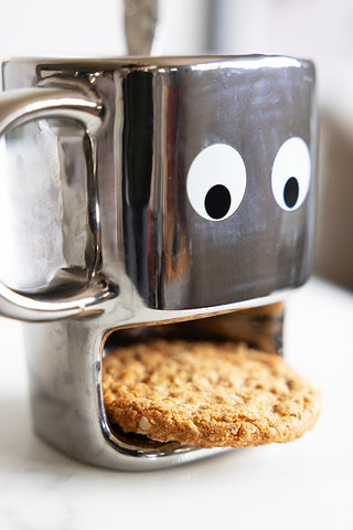 Silver novely mug with a face and a slot that is storing a hobnob biscuit.