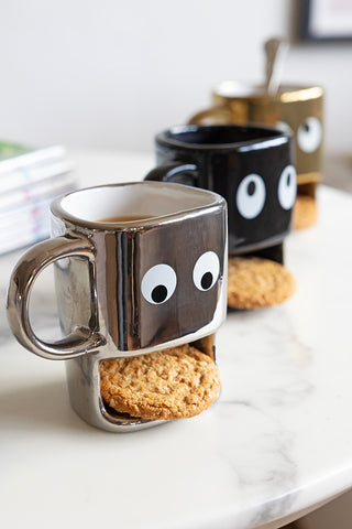 Three cookie holding face mugs in a row. At the front is the silver mug.