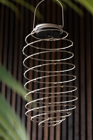 The Spiral Solar Exterior Lamp hanging in the air, styled with a plant.