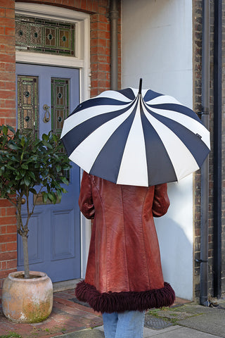 Lifestyle image of the Statement Black & White Umbrella being held outside a town house with a blue door.