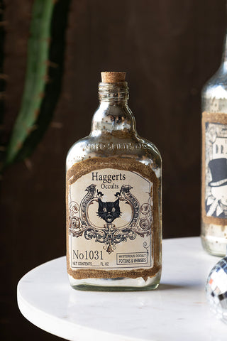 The Vintage-Style Occult Ornamental Glass Bottle styled on a table with another bottle and a disco ball, with a cactus in the background.