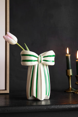 The White & Green Beautiful Bow Bud Vase with a tulip inside, styled on a black sideboard with an art print and some lit candles in candlestick holders.