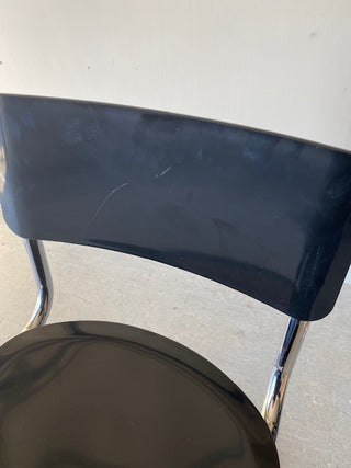 Angled view of a black chair against a white background showing a larger scratch on the backrest