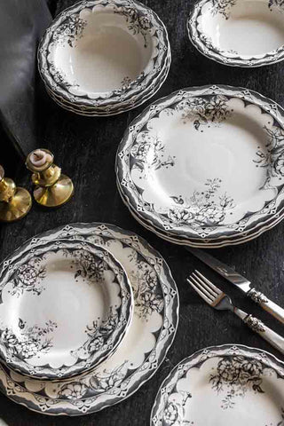 The 12-Piece Vintage-Style Floral & Star Dinner Set displayed on a black table with a knife and fork and some gold candlestick holders.
