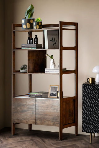 The Acacia Wood & Marble Display Cabinet styled with various accessories and plants on in front of a neutral wall, next to a sideboard.