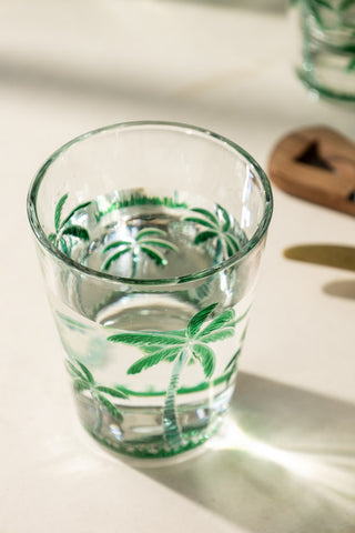 A close up of a green palm tree acrylic tumbler glass with water in it. 