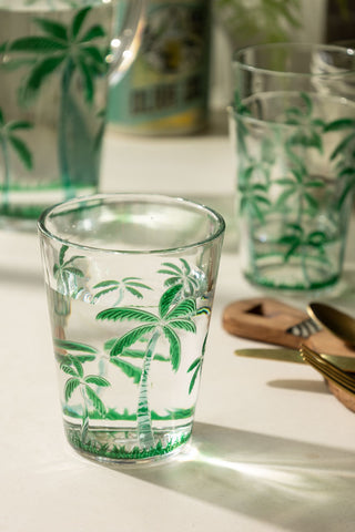 A lifestyle image of an acrylic green palm tree tumbler glass with a few more stacked behind it.