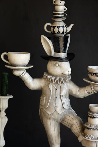 A quirky white rabbit ornament balancing tea cups in it arms and on its top hat.