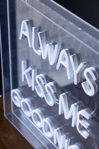 The Always Kiss Me Goodnight Neon Light Box switched off and displayed on a wooden unit.