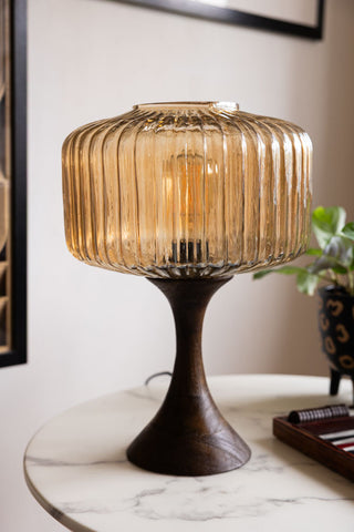 A table lamp featuring a ribbed amber glass lampshade and curved wooden stem with wide-footed base