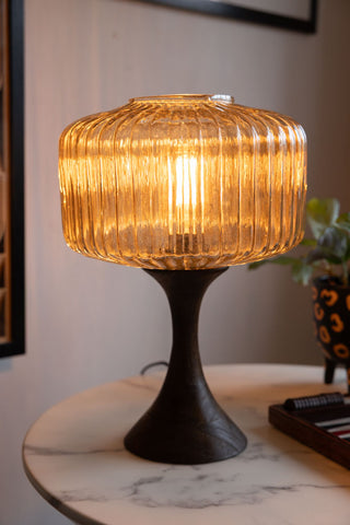 A brightly lit table lamp made from ribbed amber glass and a curved wooden base