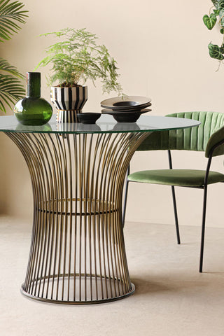 The Bronze & Glass Round Dining Table styled with a green dining chair, plants and several accessories.