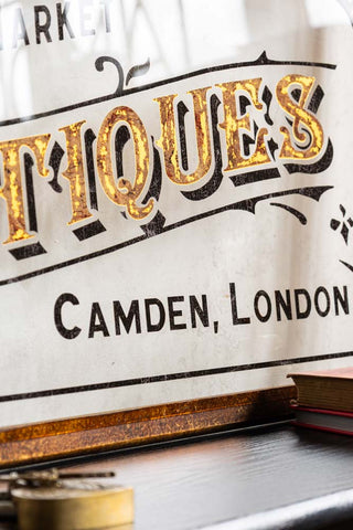 Close-up of the Antique-Style Gold Framed Stables Market Wall Art styled behind some books and accessories on a wooden surface.