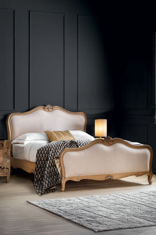 The Antique-Style Luxury Linen & Wooden Bedframe in a bedroom, styled with bedding, pillows, a rug, bedside table and lamp.